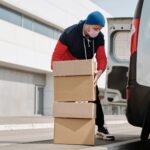 Delivery worker wearing a face mask loads boxes into a van, reflecting pandemic precautions.