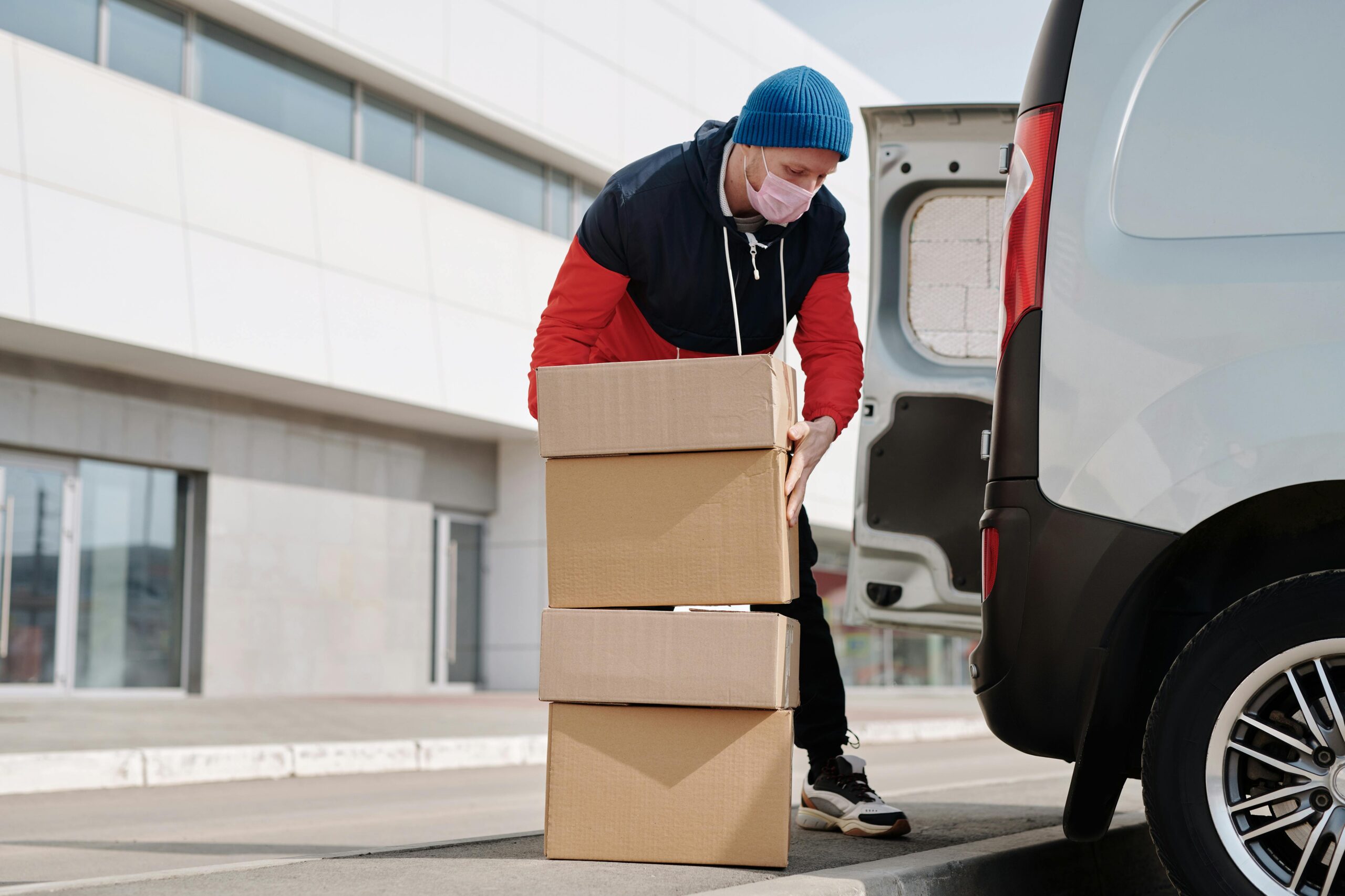 Delivery worker wearing a face mask loads boxes into a van, reflecting pandemic precautions.